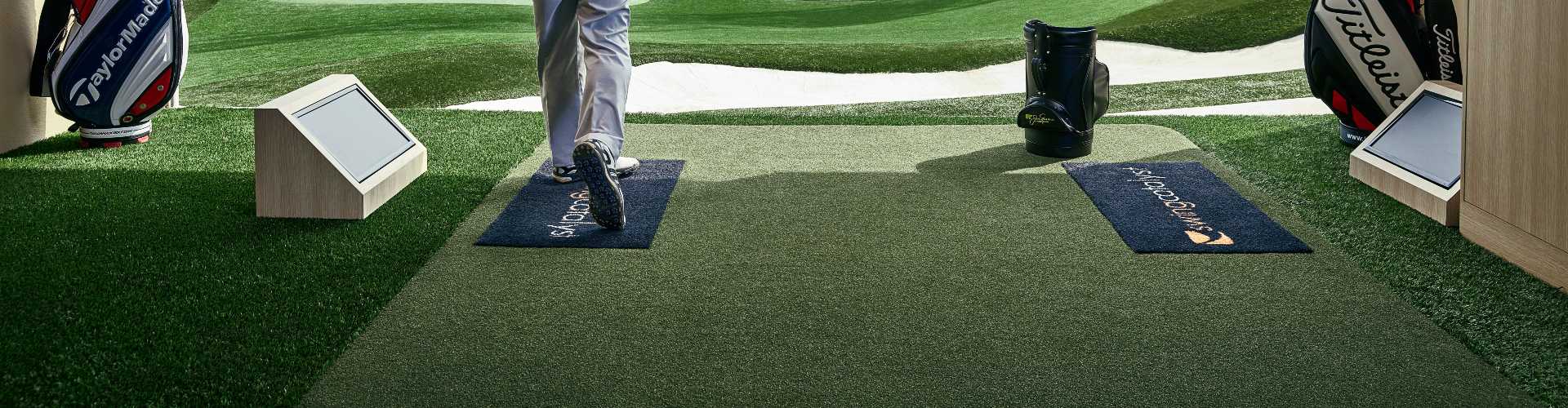 Golfer standing on Southwest Greens tee lines at a golf studio with two hitting bays and a course in the background